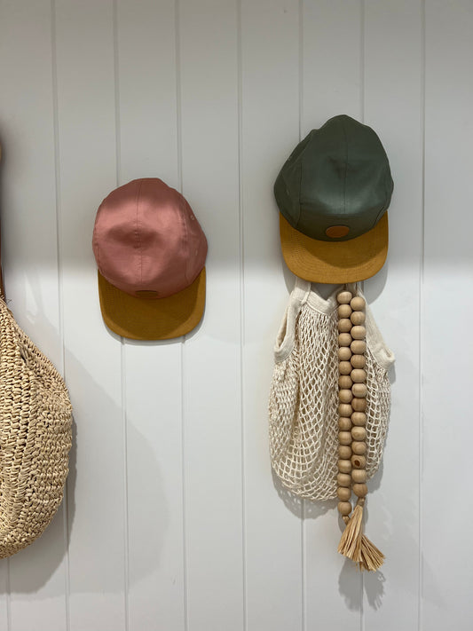Ombra & Sole UPF50+ pink and green kids sun hats hanging on a wall — stylish sun protection for everyday family adventures.