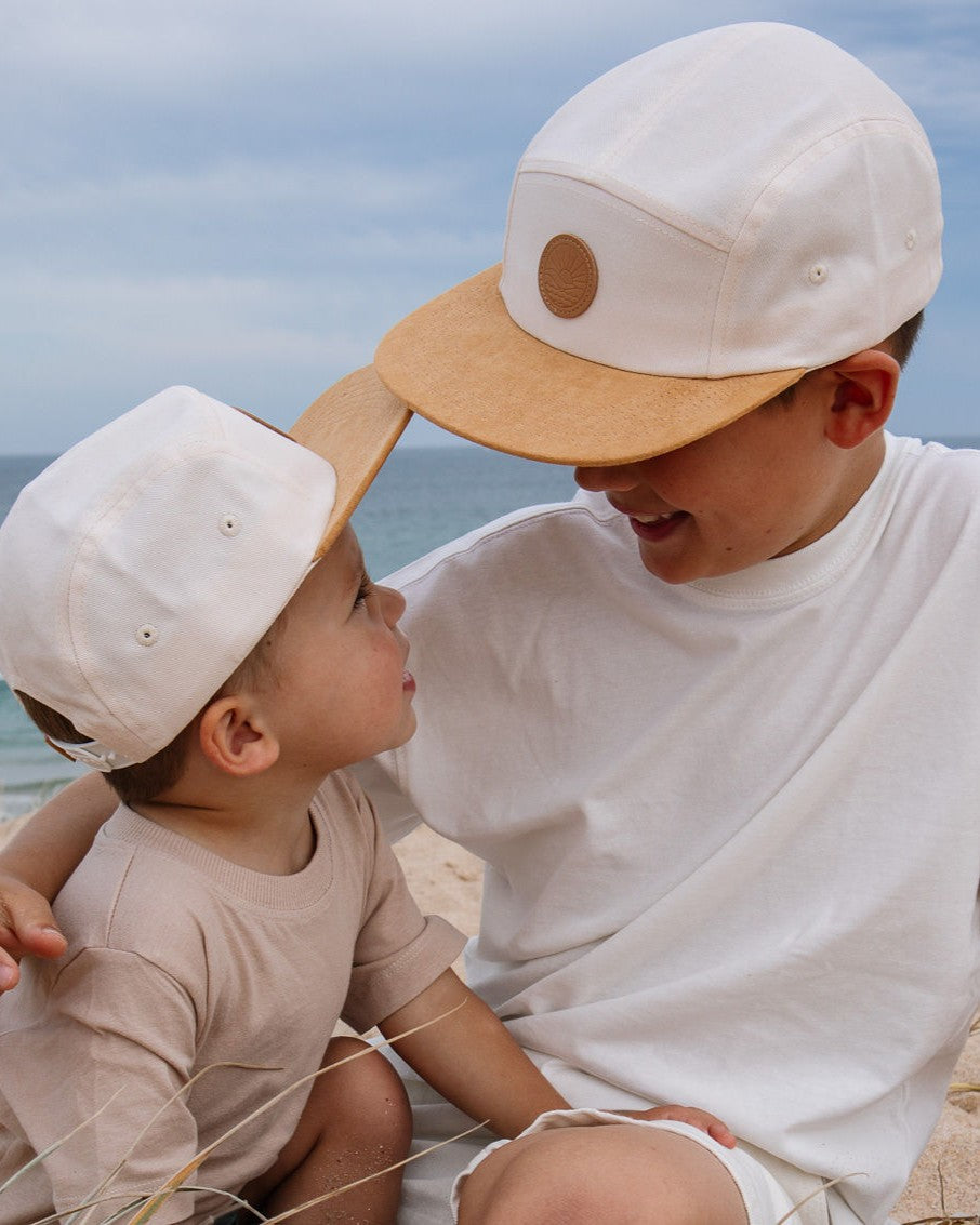 Two brothers wearing matching cream Ombra & Sole UPF50+ 5 panel hats on an Australian beach — stylish sun safe hats for kids and the whole family