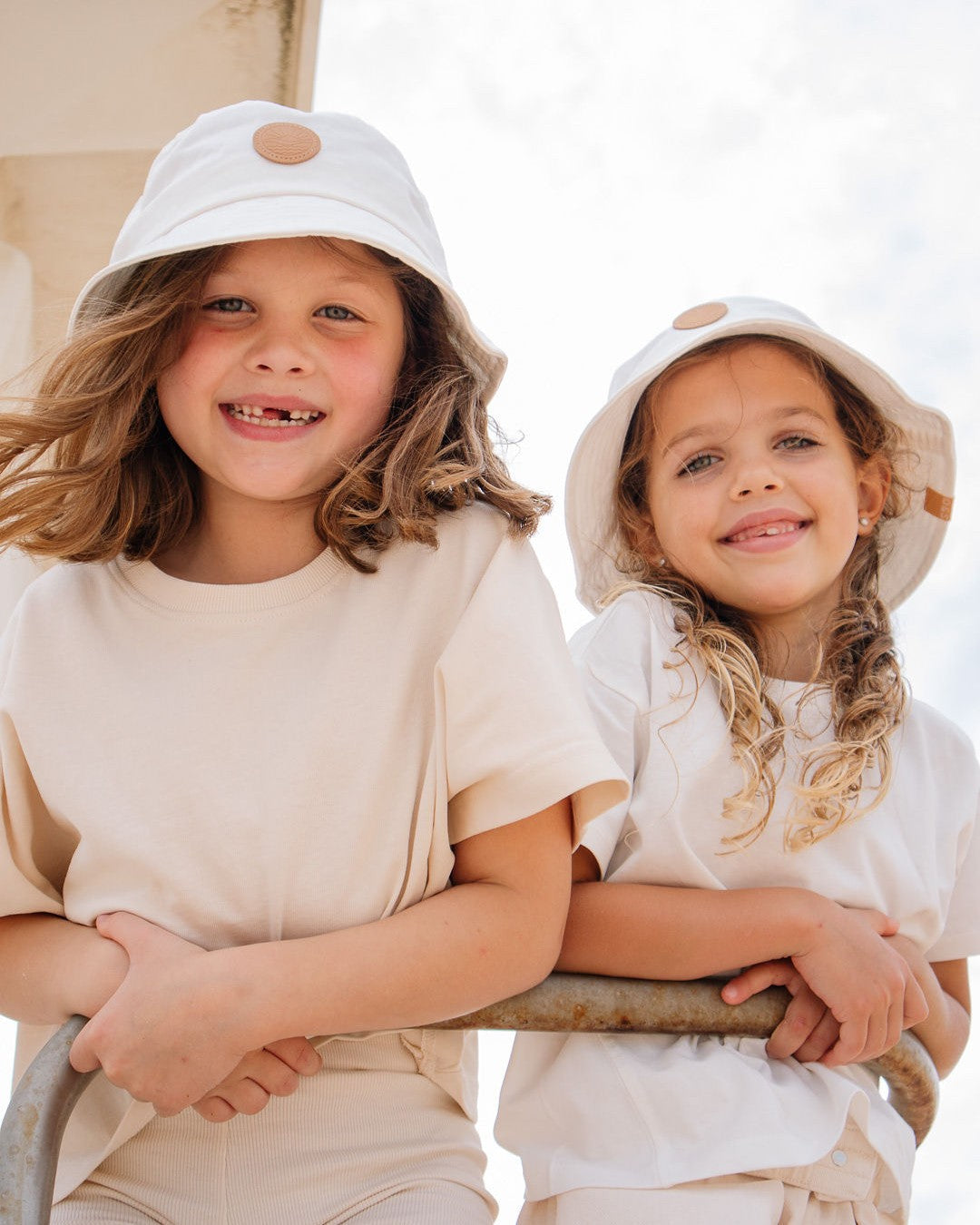 two girls at the beach with white bucket hats on, ombra and sole uPF50+ cotton bucket hats, smiling, wearing cream and white clothes